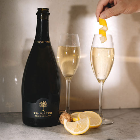 Tempus Two Blanc De Blanche varietal poured into two glasses with a lemon peel to garnish