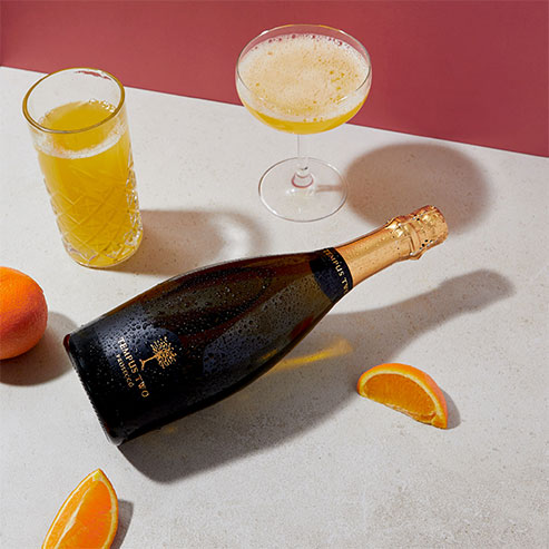 Bottle of Tempus Two Prosecco next to a mimosa cocktail with orange slices