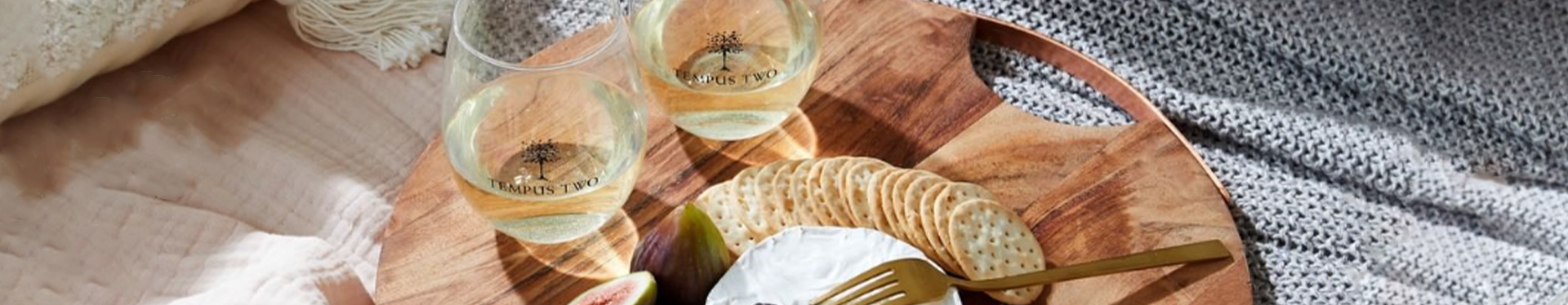 Two glasses of Tempus Two white wine varietal next to a charcuterie board containing cheese, figs and crackers